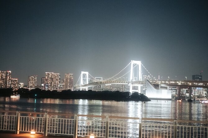 A white suspension bridge lit across the bay, seen from the waterfront rail