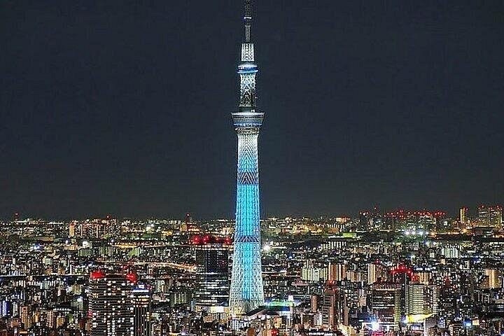 A tall broadcast tower lit pale blue above the city lights at night