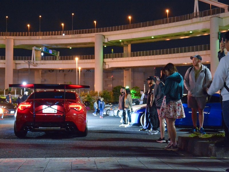 Cars and onlookers at the car meet beneath the curving expressway ramps