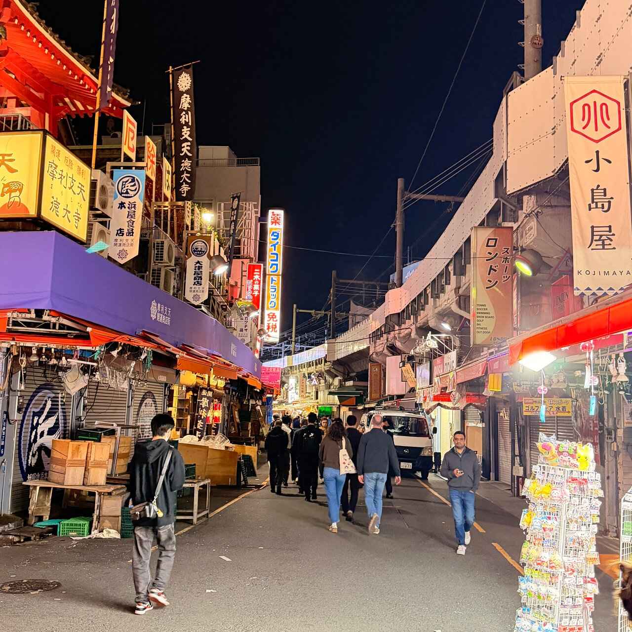 A lane of bars and food stalls beside the railway tracks after dark