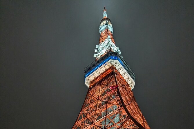 Looking up the lit lattice of a red and white tower at night